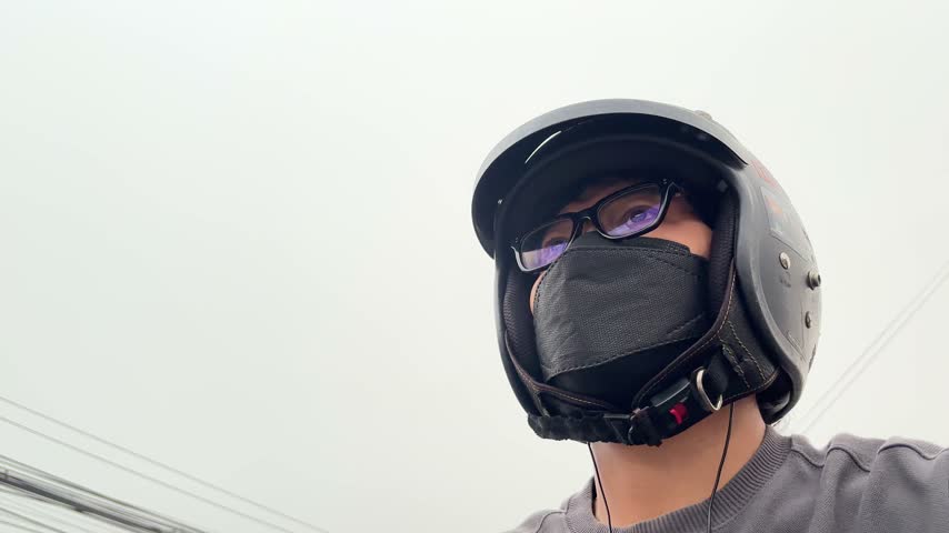 Low angle POV view of a man wearing a motorcycle helmet, glasses, and face mask while riding outdoors. Asian male rider wearing protective gear helmet and face mask during daily commute