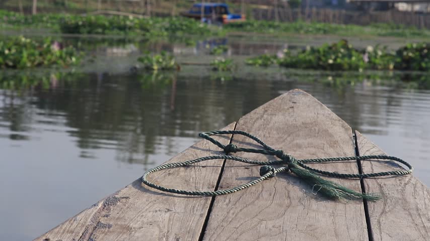 Close view of weathered wooden dock and fishing net on calm lake water with reflections and shoreline greenery in background.