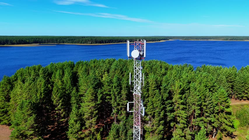 Telecommunication tower standing tall amidst vibrant green pine trees by a calm blue lake