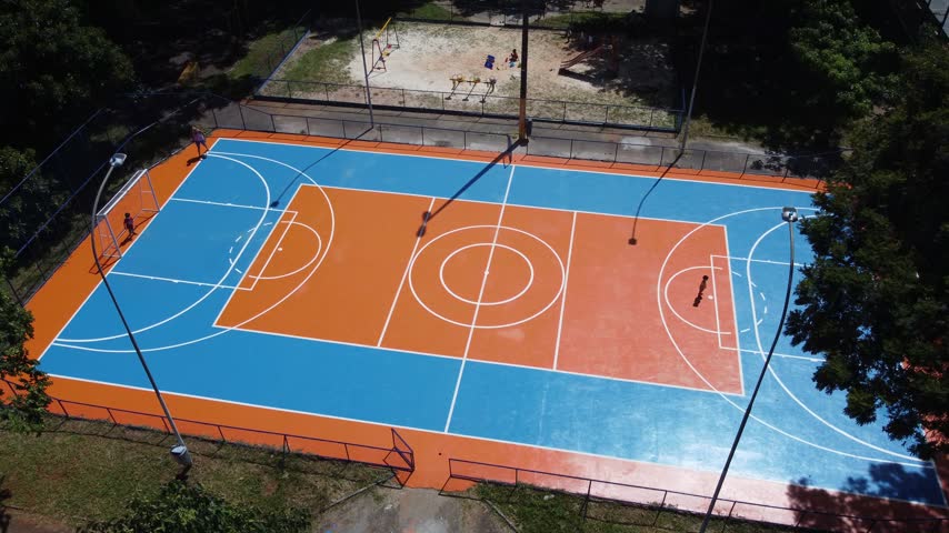 Brightly colored outdoor sports court in Brasilia, Brazil, with families using the public recreation facility surrounded by trees and open space, aerial view