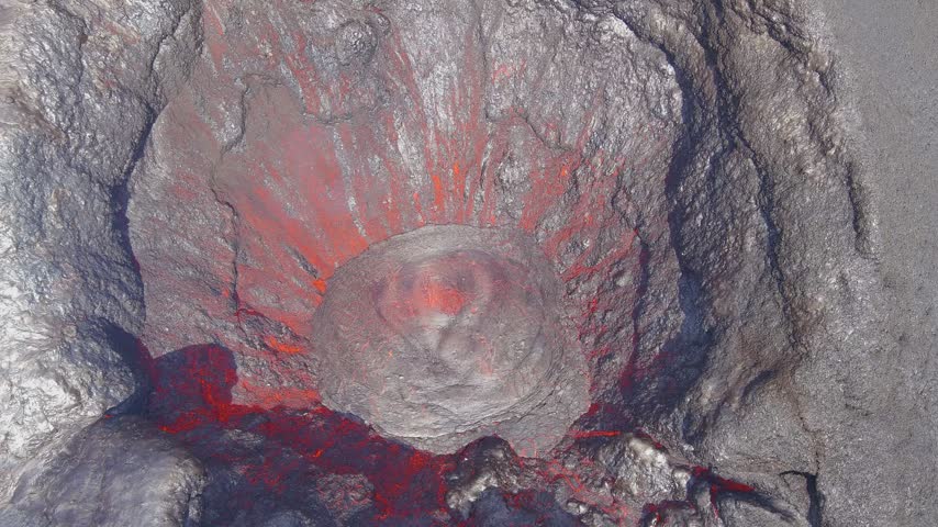 Aerial view of a volcanic crater with a glowing lava lake and flowing molten rock.
