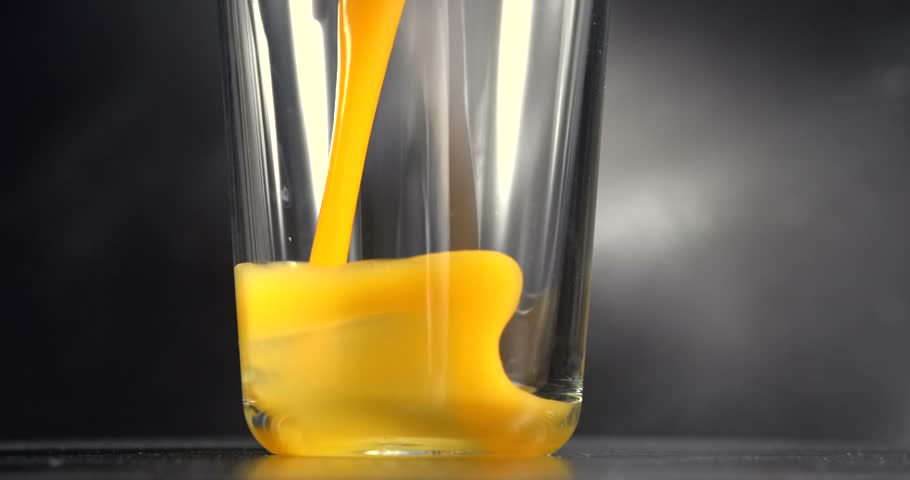Orange juice pouring into glass in slow motion on black background
