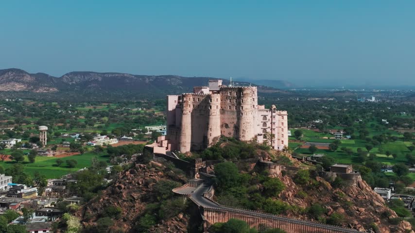 Aerial of Bishangarh Fort, a 230-year-old warrior fortress built in the late 18th century by Rao Bishan Singh. The sandstone structure sits atop a rocky hill surrounded by green agricultural fields.
