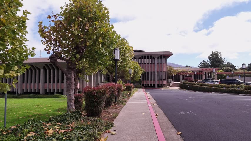 Modernist architecture of the City Hall in Daly City, California, showing its unique facade, landscaped garden, and entrance on a partly cloudy day with beautiful trees and plants