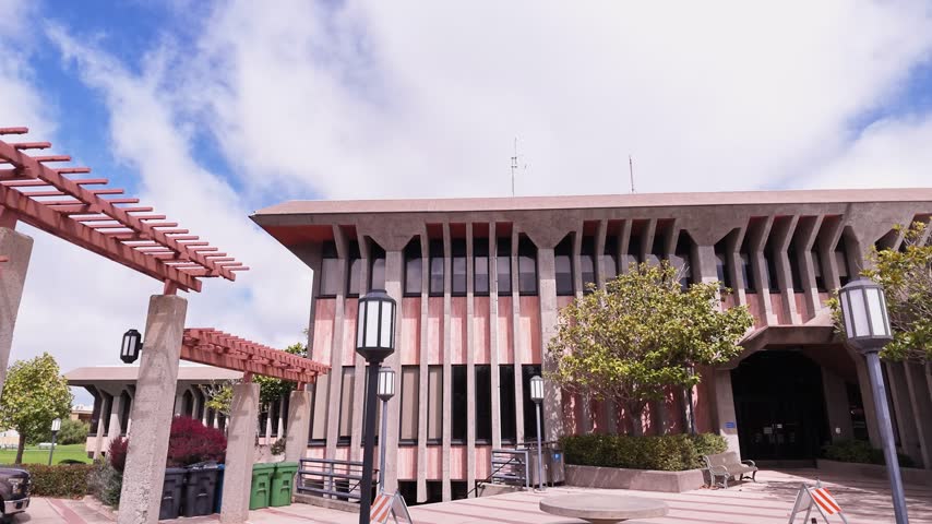 Panning shot of the exterior facade of the Daly City Hall building, a prominent civic government and administrative center located in San Mateo County under a beautiful blue sky with clouds