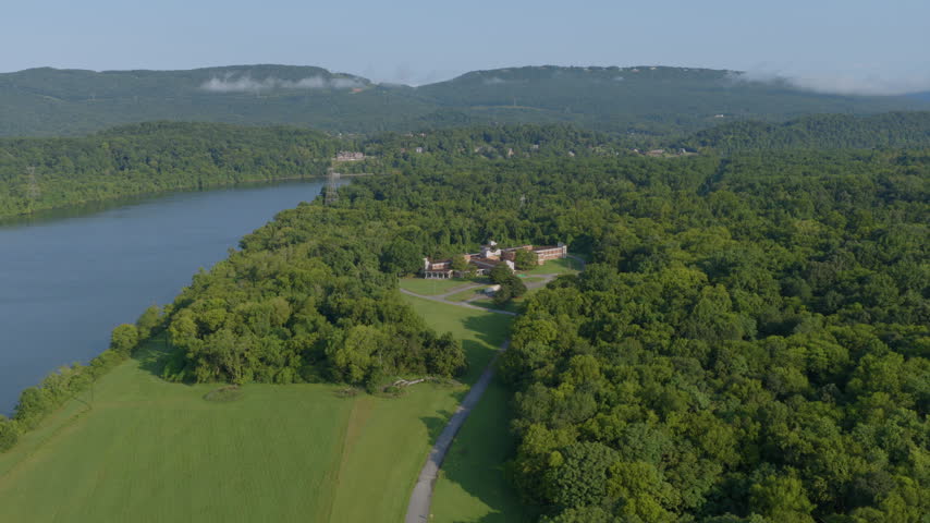 Drone shot of a riverside building nestled among dense forest along the Tennessee River near Chattanooga, with mountains beyond.