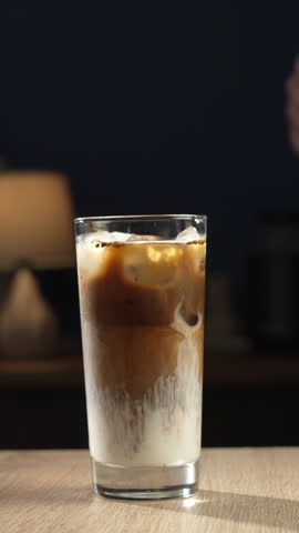 Bartender mixing iced latte in glass with ice on bar counter, close-up