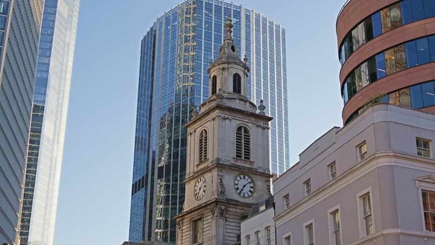 Architectural contrast between traditional stone church tower and contemporary glass office buildings in London city.