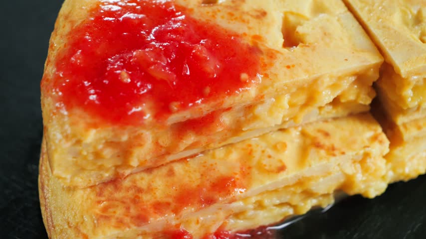 Close up of Spanish potato omelette Tortilla de patatas slices topped with grated tomato, a traditional Spanish dish. 