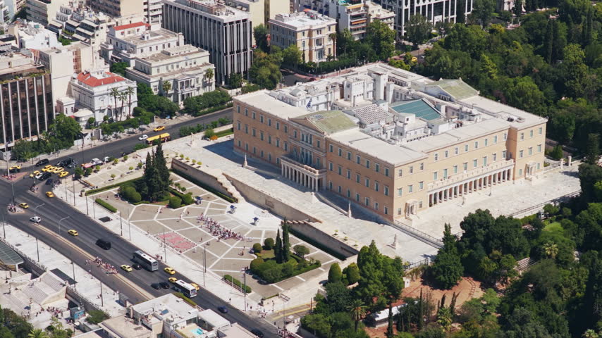 High-angle aerial view of the historic Hellenic Parliament building and Syntagma Square in the city center of Athens, Greece, with urban traffic moving on a sunny day