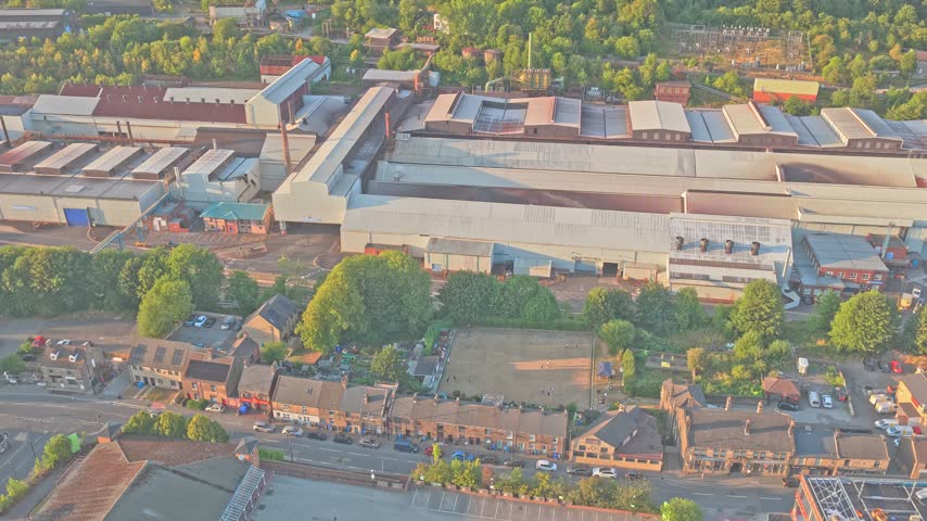 Stocksbridge steelworks with extensive production halls beside residential streets and woodland, Upper Don valley, South Yorkshire, England, drone ascent.