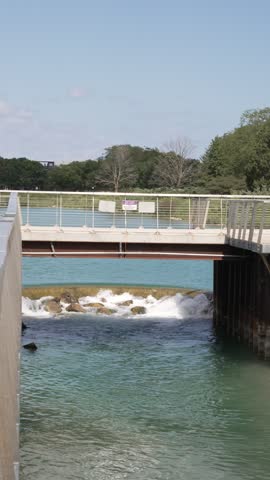 Vertical video view of a small dam on a lake with a bridge crossing above, surrounded by calm water and natural scenery
