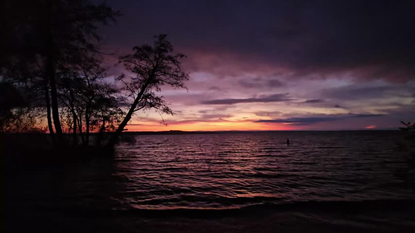 Scenic sunset over a massive reservoir lake in autumn with alder trees and colorful cloudy sky at dusk