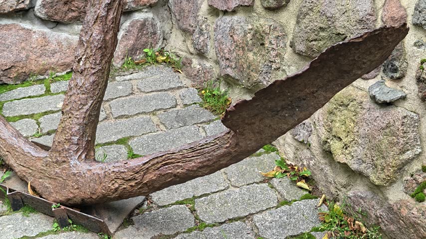 A large anchor sits on top of a brick sidewalk.