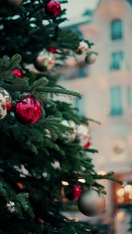 Festive holiday evergreen tree with glowing lights and vibrant red and silver ornaments swinging slowly in twilight setting.