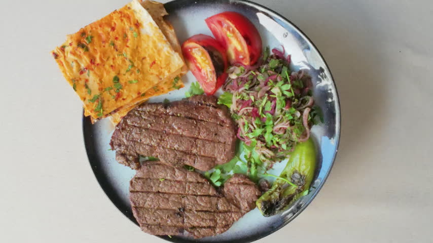 Plate with grilled beef steak, fresh salad, tomatoes, pepper, and flatbread rotating top view