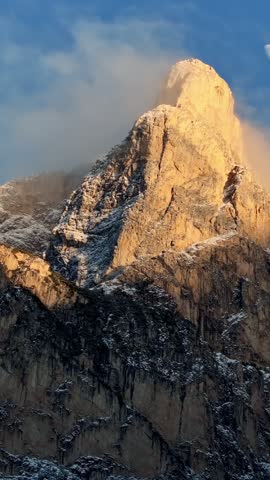 Time lapse footage featuring moon movement over rugged rocky mountain summit bathed in warm golden light during winter dusk atmospheric phenomenon.