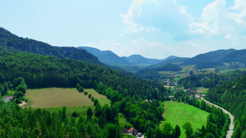 Scenic view of a landscape with hills and fields in a rural area. The landscape shows hills, green fields, and trees in a rural area under a blue sky.