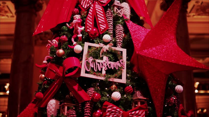 Close up of cinematic Christmas tree ornaments including red star and festive signage on green pine branches.