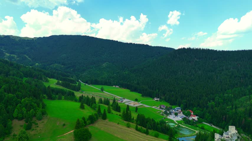 Green landscape with mountains and a small settlement in the valley on a cloudy day. The view shows rolling green hills, trees, and a small settlement nestled in the valley.