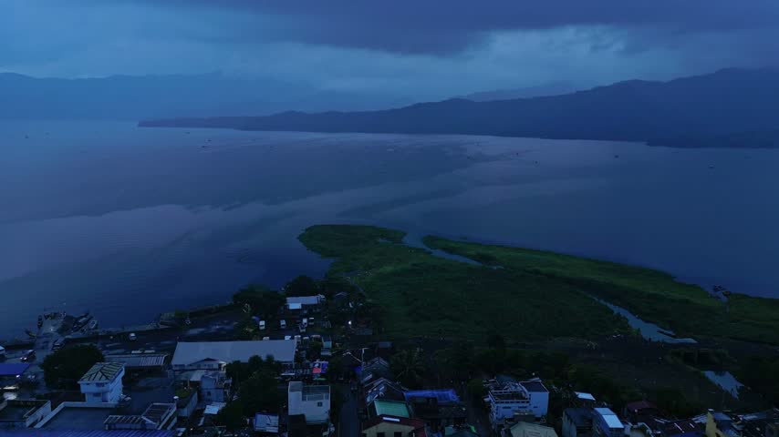 Aerial view over Buhi town and Lake Buhi at dusk in Camarines Sur, Philippines, with Mount Asog, also known as Mount Iriga, in the background. Santa Cruz barangay is visible in the distant landscape.