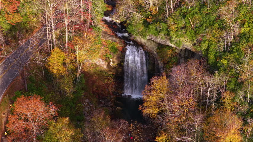 Aerial landscape of mountain waterfall, forest staircase boardwalk and scenic highway. Passing vehicles travel beside colorful autumn woodland.