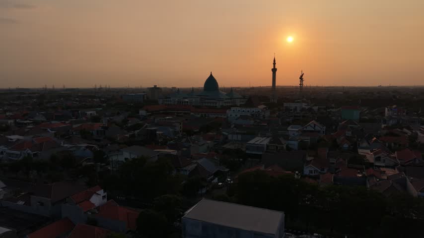 SURABAYA, INDONESIA - SEPTEMBER 23, 2026: Aerial drone view of Masjid Al Akbar Surabaya silhouetted against a vivid orange sunset sky