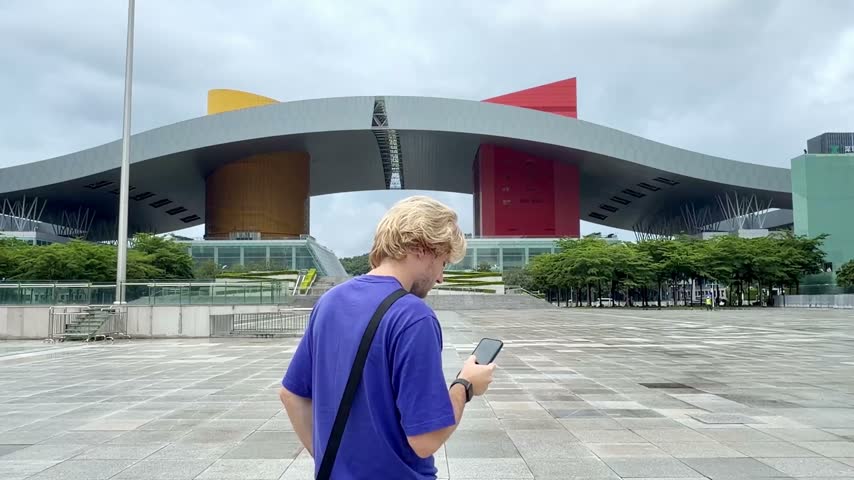 Young Man Scrolling and Photographing with Phone at Shenzhen Square	
