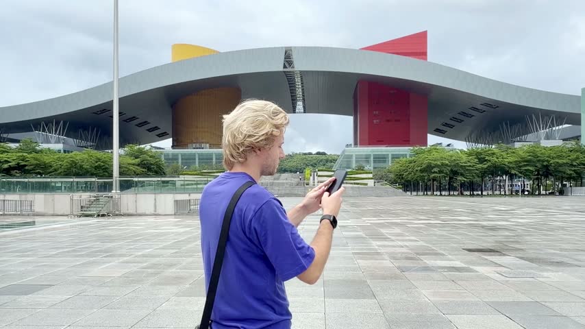 Young Man Scrolling and Photographing with Phone at Shenzhen Square	
