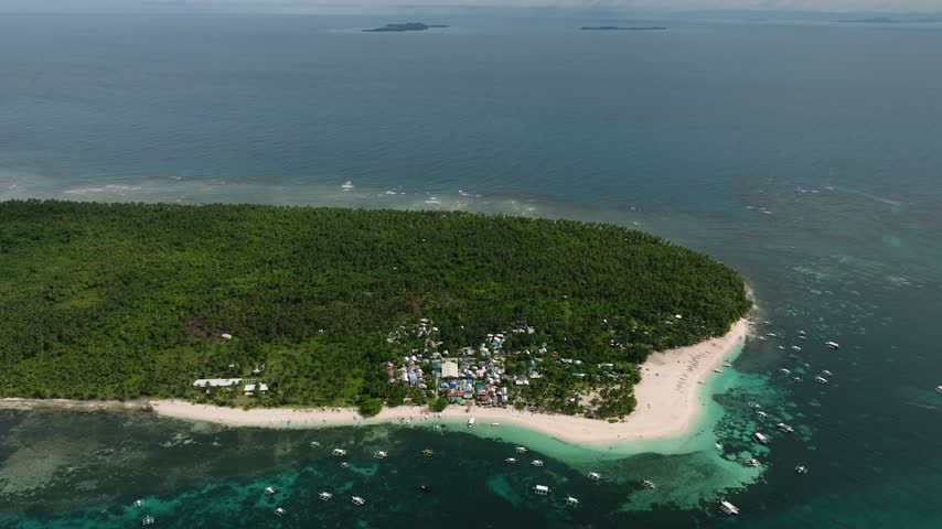 Lush island with forest interior, white sandy beach and boats near the shore. Daku Island. Siargao, Philippines.