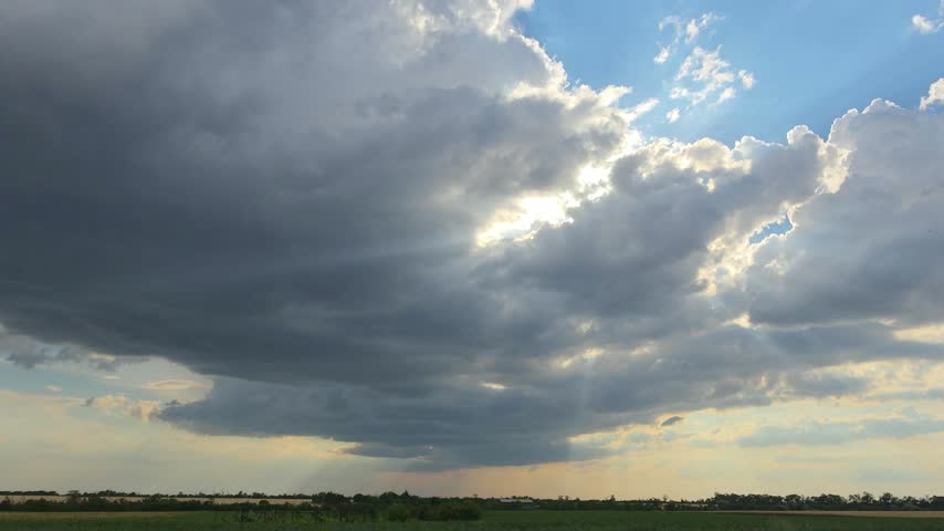 Beautiful Sunset Landscape With A Dramatic Raincloud Hanging Over An Open Field. Majestic Sunbeams Break Through The Dark Clouds Illuminating The Rural Horizon