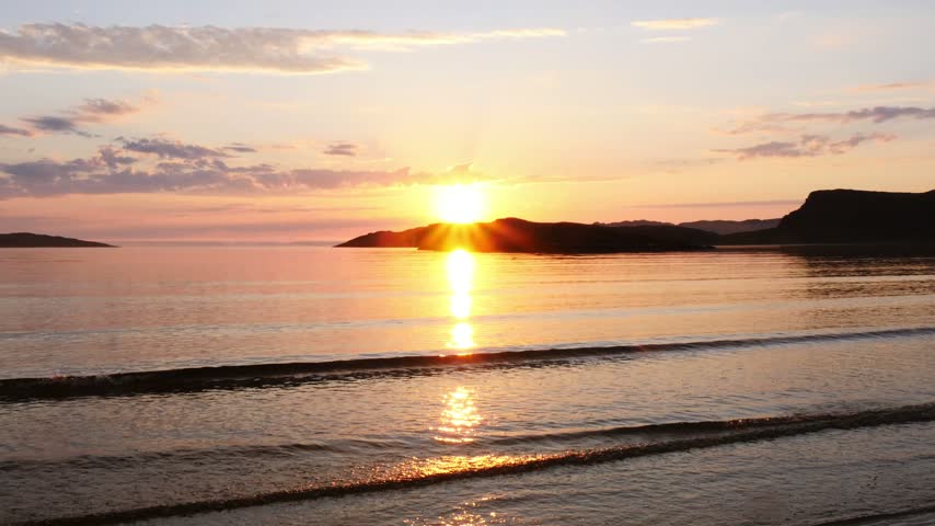 Beautiful sunset on the shores of the Barents Sea in summer during the Polar Day. The never-setting sun floats low above the horizon. Teriberka, the end of the earth.