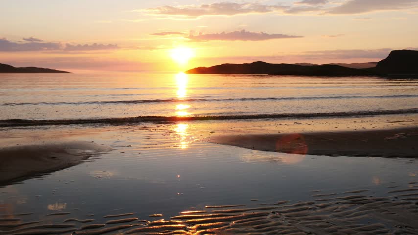Beautiful sunset on the shores of the Barents Sea in summer during the Polar Day. The never-setting sun floats low above the horizon. Teriberka, the end of the earth.