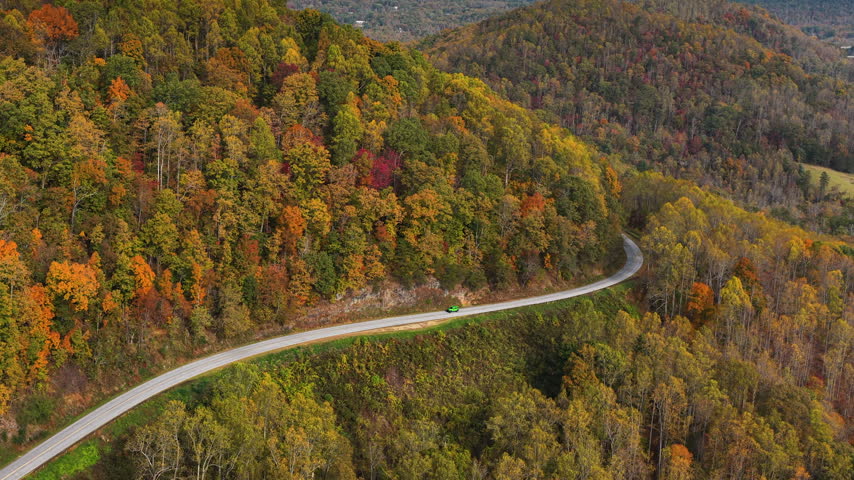 Cars driving on Blue Ridge Parkway in autumn season. Scenic route between majestic mountain hills covered in golden and scarlet leaves.