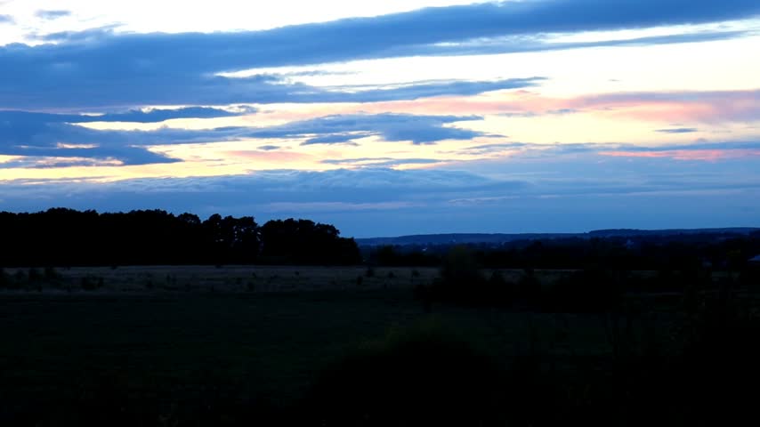 Picturesque evening landscape featuring a silhouette of a forest on the horizon under a dramatic cloudy sky during twilight. 