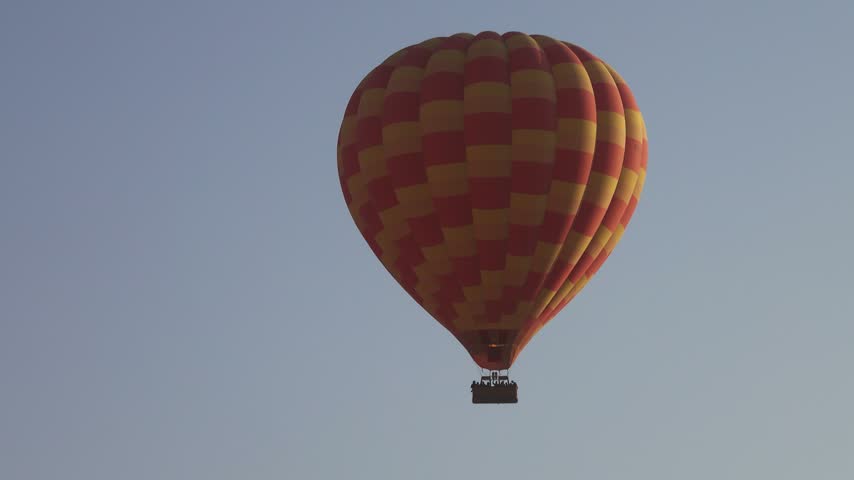 View of a colorful hot air balloon floating in the clear sky over the desert landscape of Luxor Governorate, Egypt.