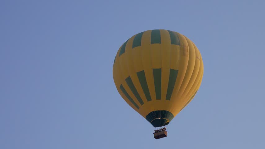 View of a yellow and green hot air balloon floating in the clear blue sky over Luxor Governorate, Egypt.