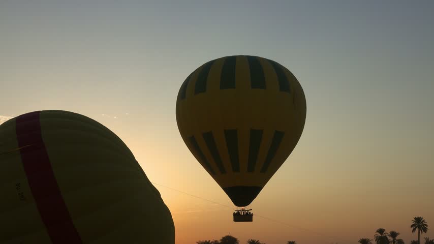 View of hot air balloons floating in the sky during sunrise over the landscape of Luxor Governorate, Egypt.