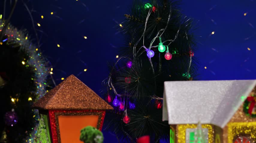 In the center of the Christmas village, a yellow car pulls up to a gray little house adorned with small fir trees and snowmen