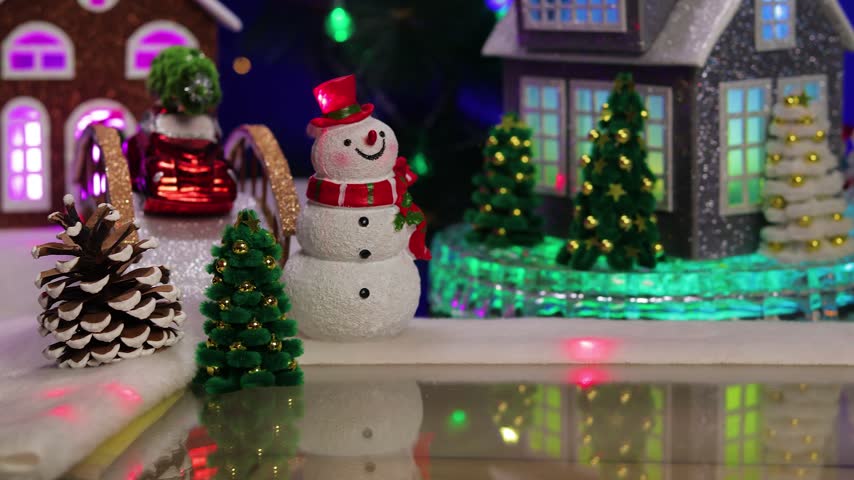 In the center of the Christmas village, a yellow car pulls up to a gray little house adorned with small fir trees and snowmen