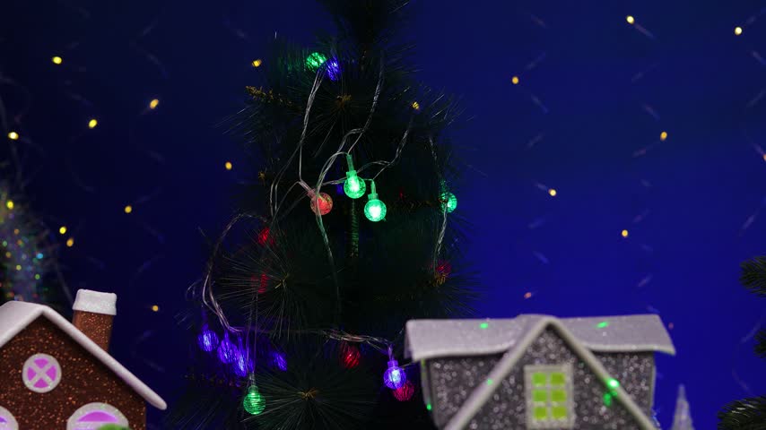 In the center of the Christmas village, a yellow car pulls up to a gray little house adorned with small fir trees and snowmen