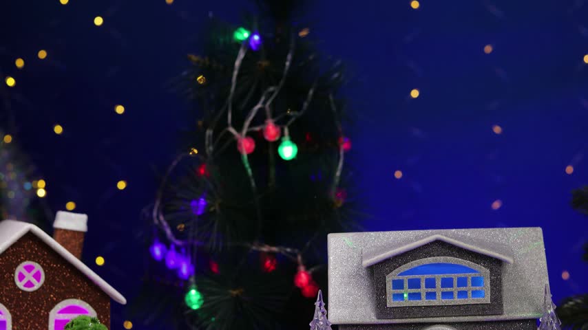 In the center of the Christmas village, a yellow car pulls up to a gray little house adorned with small fir trees and snowmen