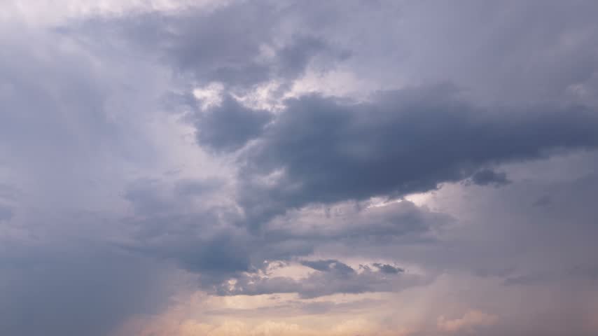 Looking upwards toward white, dark, and fluffy storm clouds forming in front of stormy blue sky as sunlight breaks through storm-clouds with lighting as shades of blue spell rain and rainfall coming