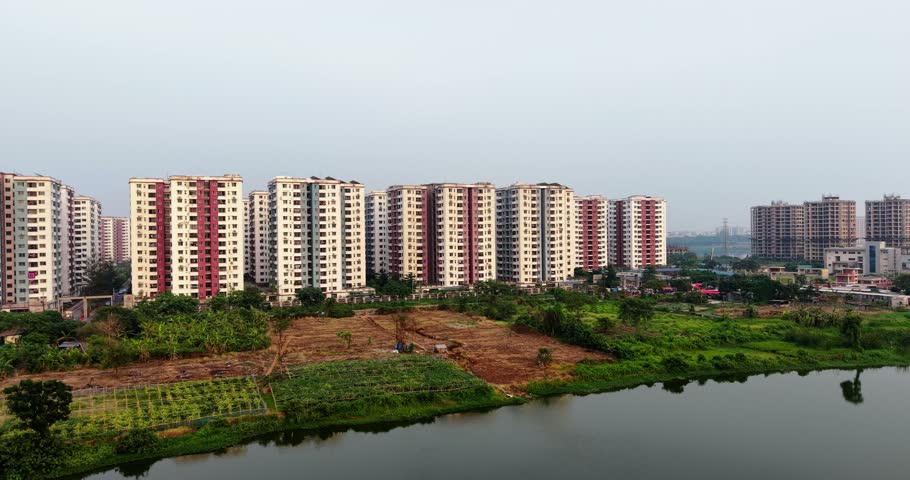 A wide aerial shot of a residential apartment complex with tall buildings situated next to a calm lake and lush green vegetation.