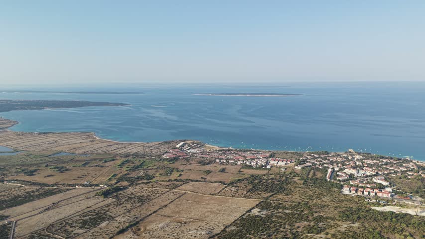 Aerial panorama of dry stone walled fields and a coastal settlement beside the blue Adriatic Sea in Croatia, in hazy sunshine.