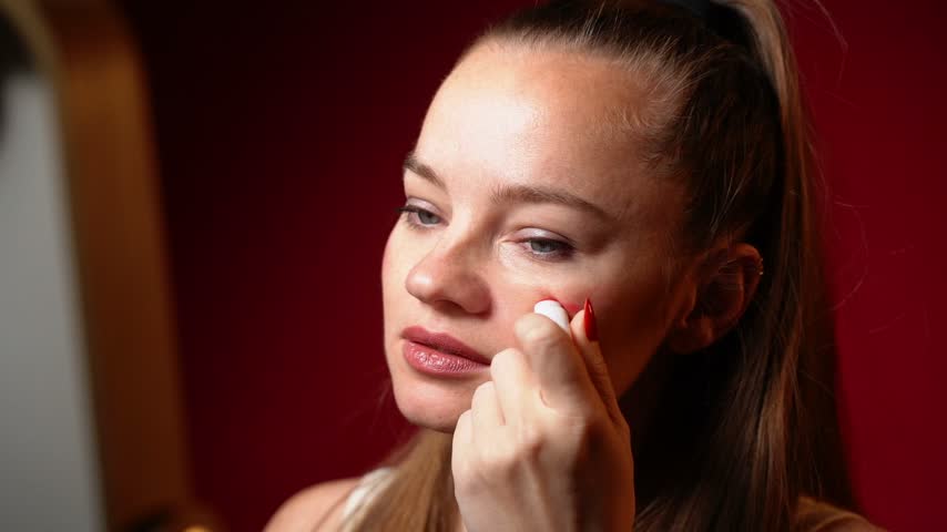 Young woman looking in a mirror and applying a colorful rainbow pride flag on her face