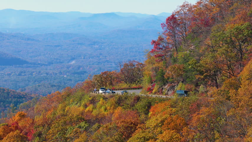 Scenic overlook in the Appalachian Mountains of Tennessee with a parked car enjoying breathtaking views of colorful autumn forest and rolling hills.