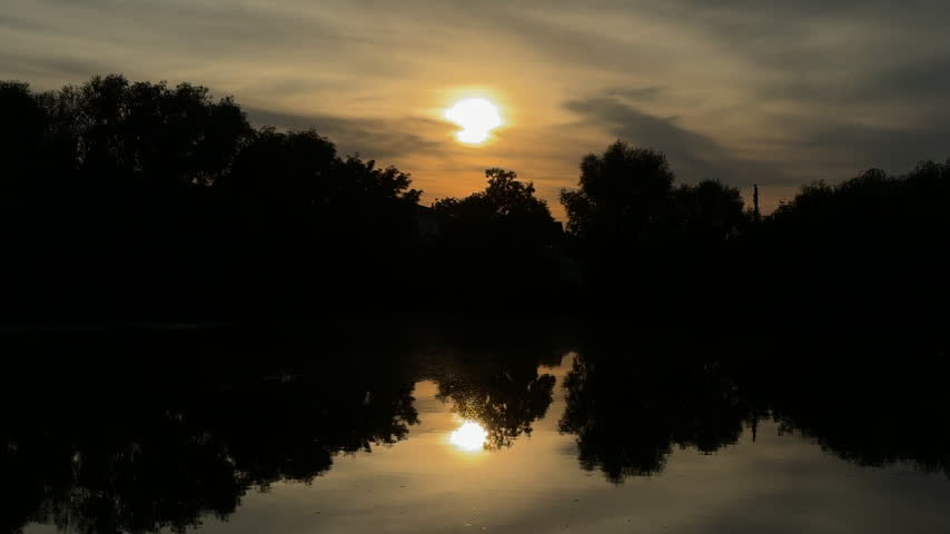 Scenic Sunset Over Calm Lake Water with Tree Silhouettes and Golden Reflections