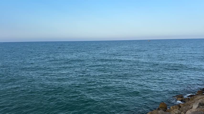 Calm open Mediterranean water stretching to an empty horizon, with dark rocks in the lower corner of the frame in Gandia, Spain.