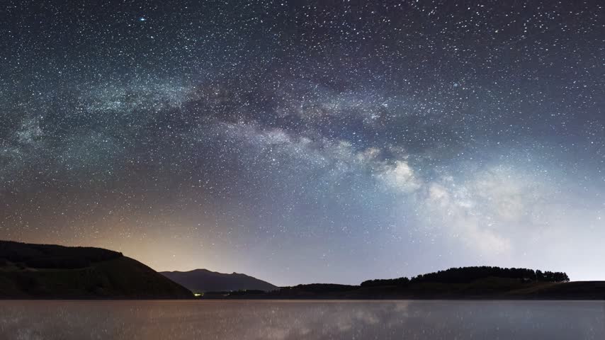 Bright colorful milky way galaxy over the small lake, forest and mountains. `night landscape. `Starry sky time lapse.